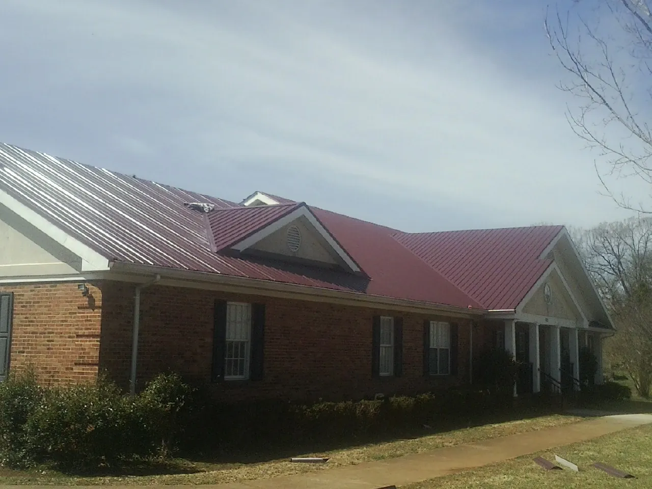Red metal roof with gabled entries on a long brick building, from a Hail Damage Roof Repair job in Pauline