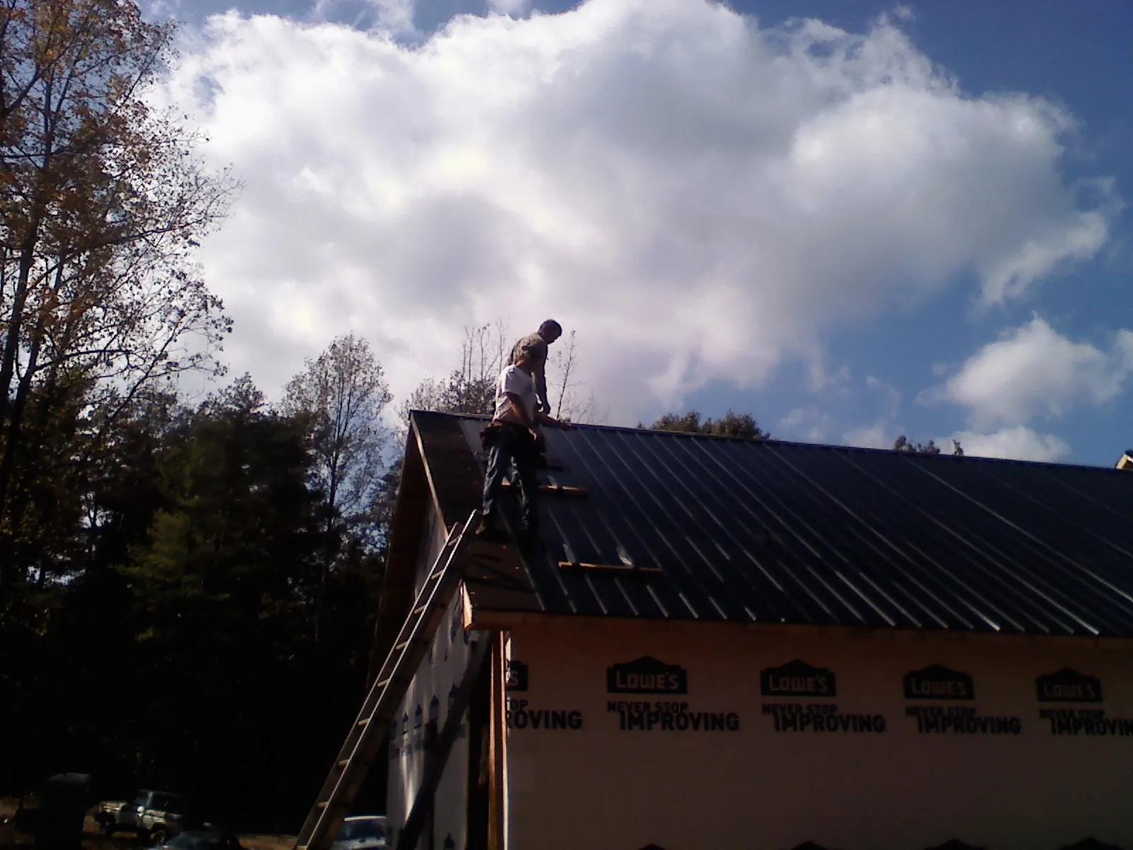 Roofer fastening dark metal panels high against a cloudy sky, from a Roof Inspection job in Pauline