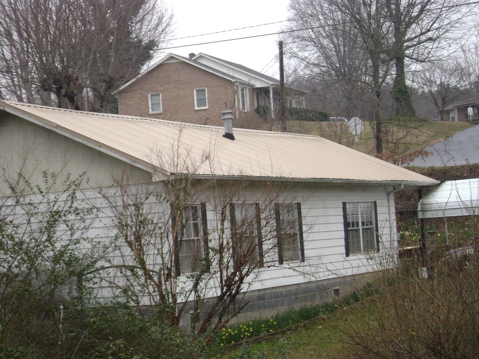 Tan metal roof on a white sided house set into a hillside — Commercial Roofing by Roofing Brothers in Pauline